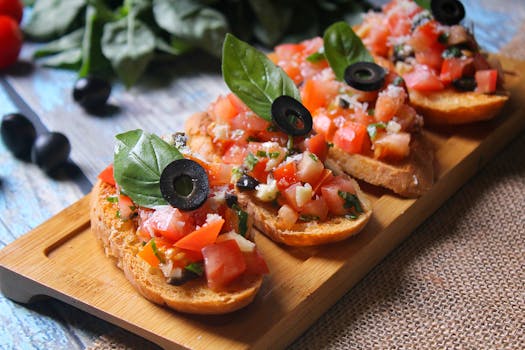Brouillettes garnies de tomates, olives et basilic sur une planche en bois, avec des ingrédients frais en arrière-plan.