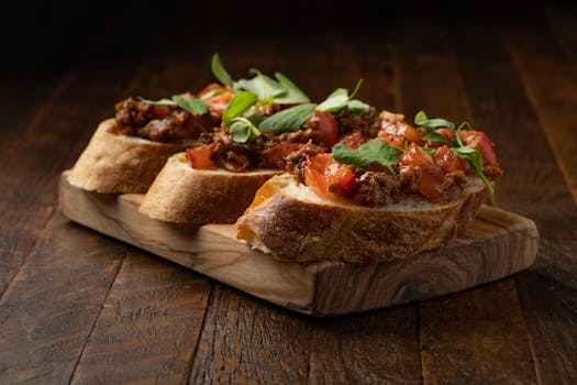 Tranches de pain garnies de tapenade, tomates et herbes fraîches sur une planche en bois.