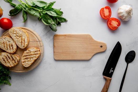 Planche en bois avec du pain grillé, tomates, ail et herbes fraîches sur un plan de travail en marbre.